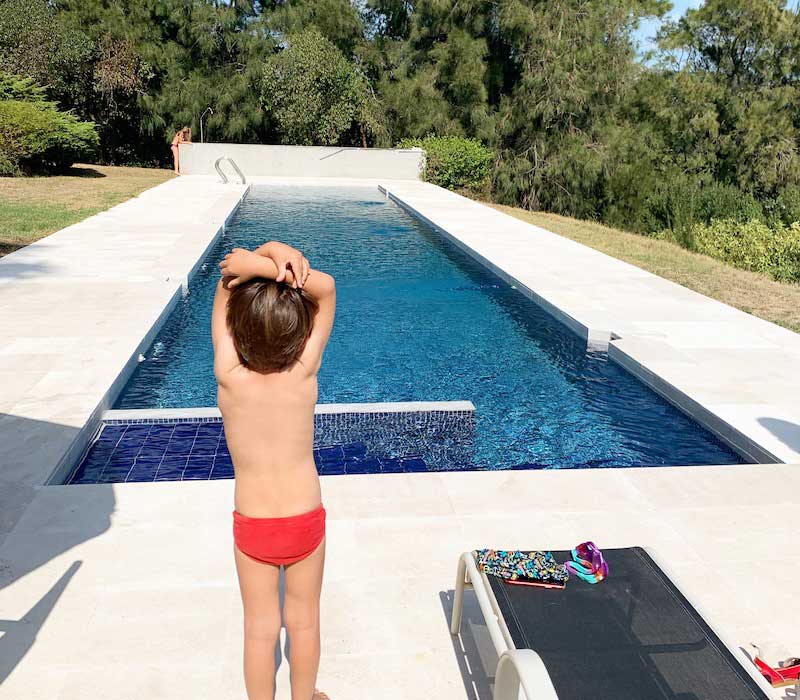Niño pequeño en bañador preparandose para zambullirse en una piscina y nadar.
