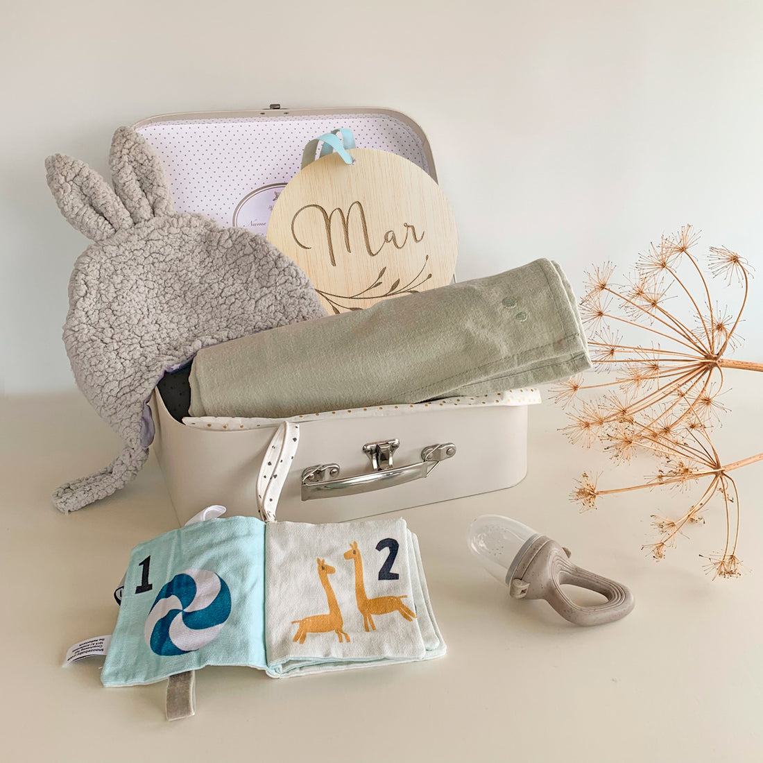 Cajita regalo bebe que incluye gorrito, muselina, libro de actividades, chupete alimentador y placa con nombre del bebé