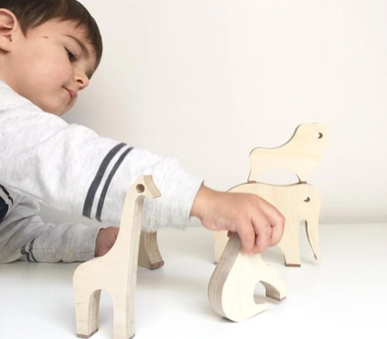 Niño jugando con animales de madera. Un león, un elefante, una jirafa y un gorila.