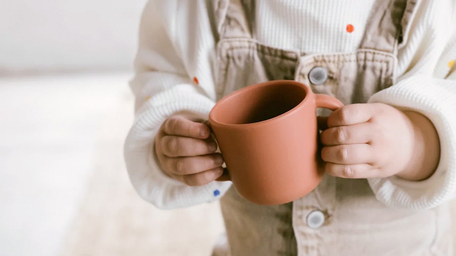 Niño sujetando un vaso de silicona con asas de color terracota
